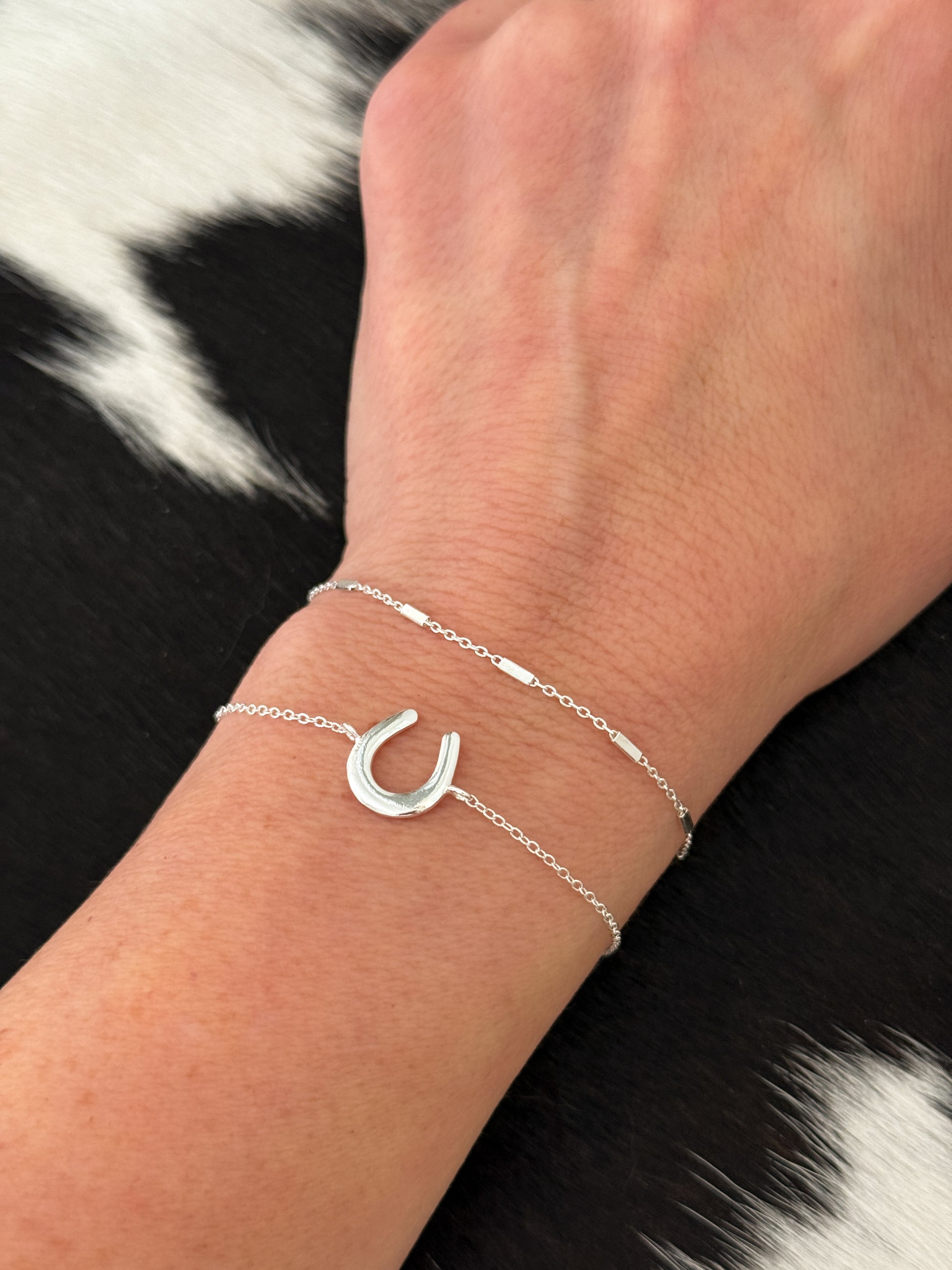 Silver bracelet with a horseshoe charm on a wrist against a black and white fur background