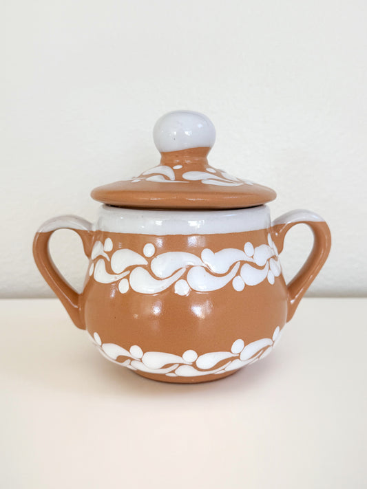 Ceramic sugar bowl with white floral patterns on a beige background