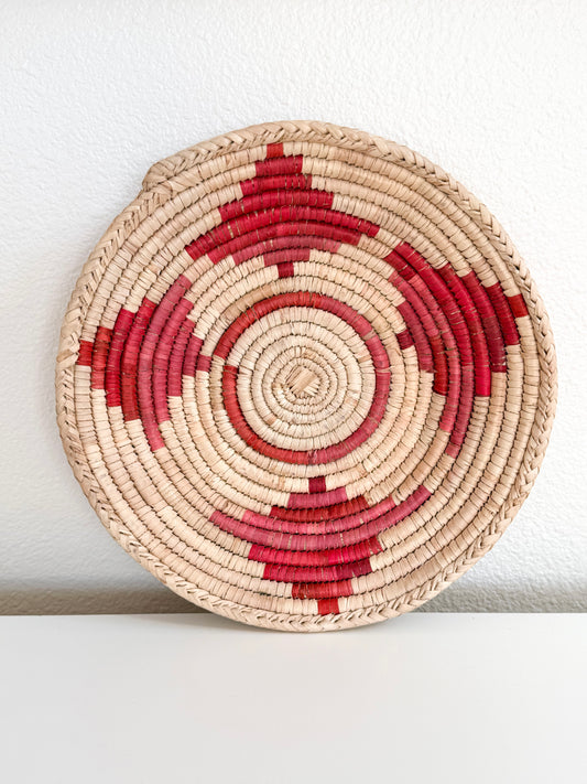 Round woven basket with red and beige pattern on a white surface