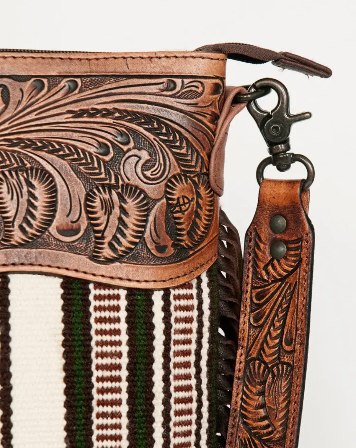 Close-up of a leather bag with intricate patterns and a strap on a striped background