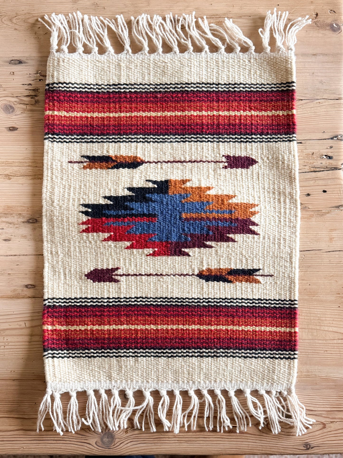 Woven rug with geometric pattern and fringes on a wooden surface