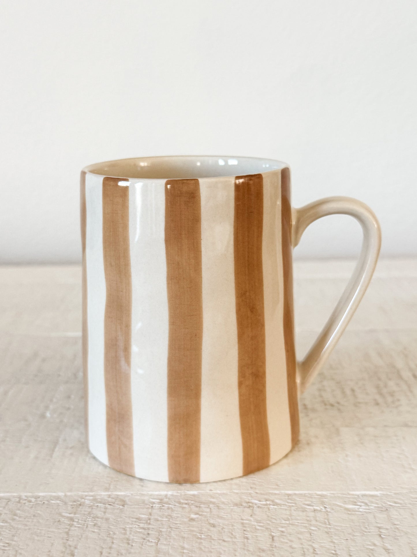 Mug with brown and white vertical stripes on a light wooden surface.