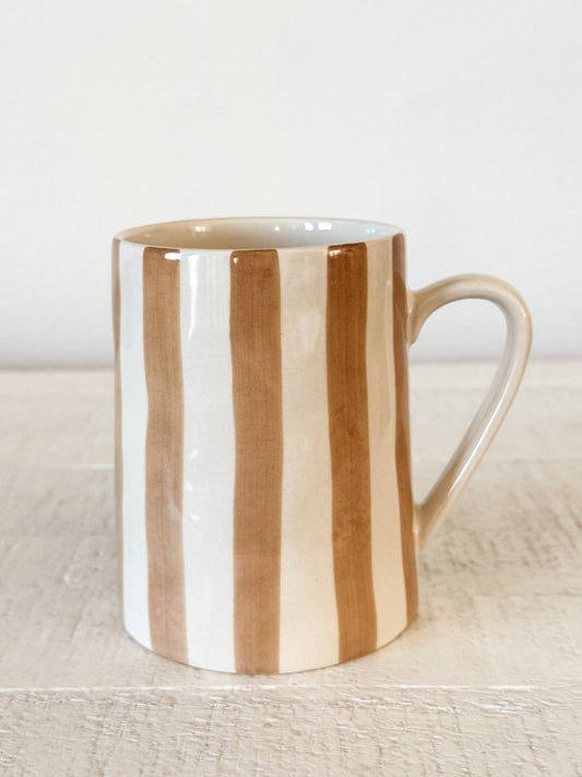 Mug with brown and white vertical stripes on a light wooden surface.