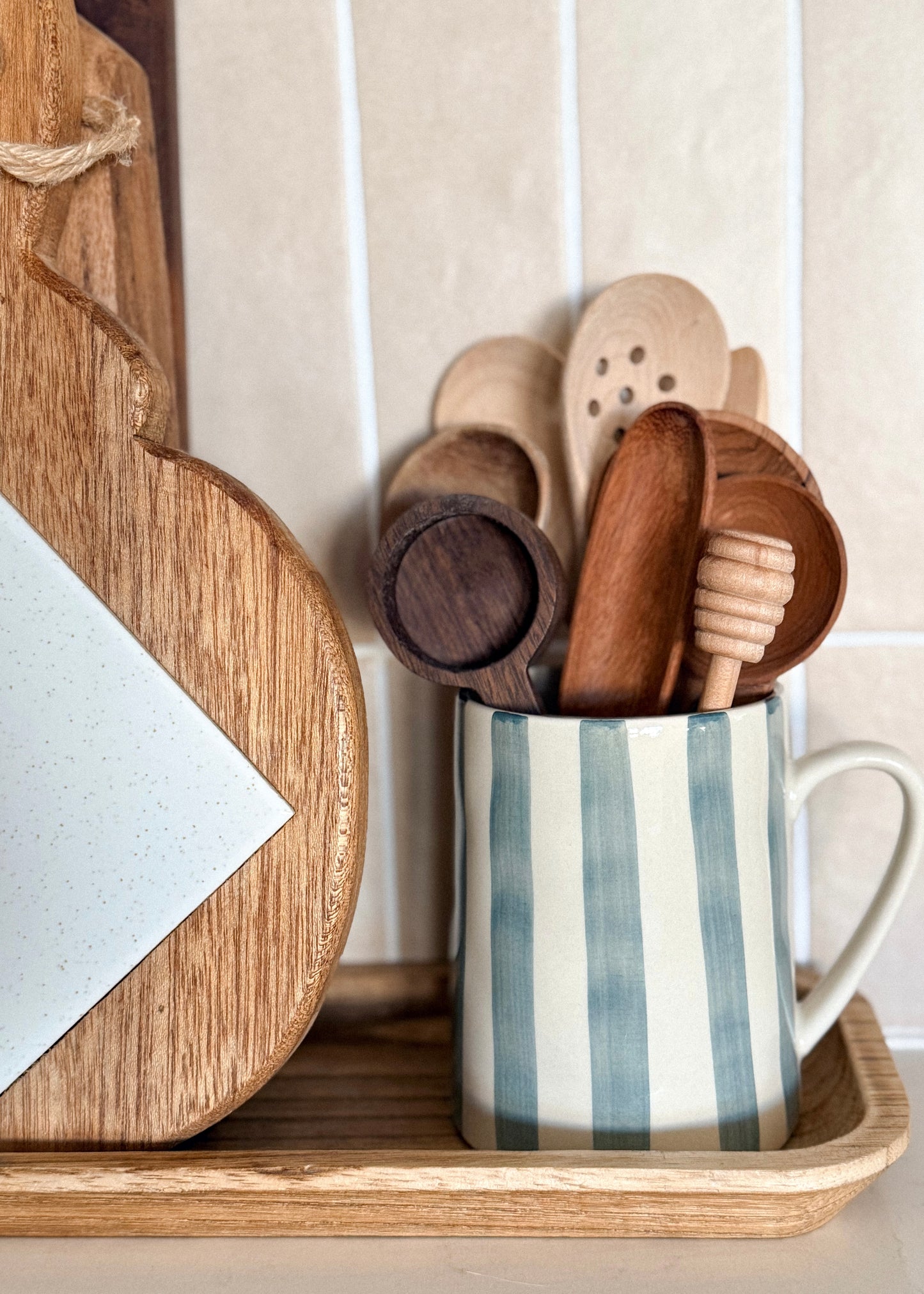 Blue stripe stoneware mug styled as a utensil holder with wooden spoons in a neutral cottage-inspired kitchen setting.