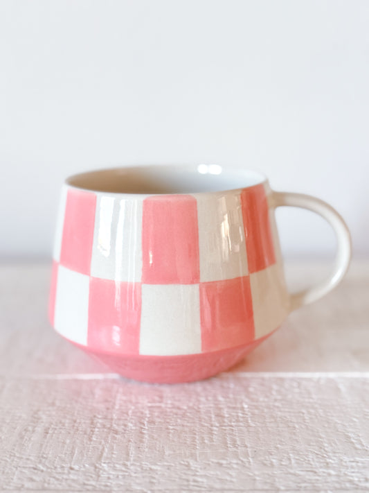 Blush pink checkered stoneware mug with hand-painted ceramic design on neutral background