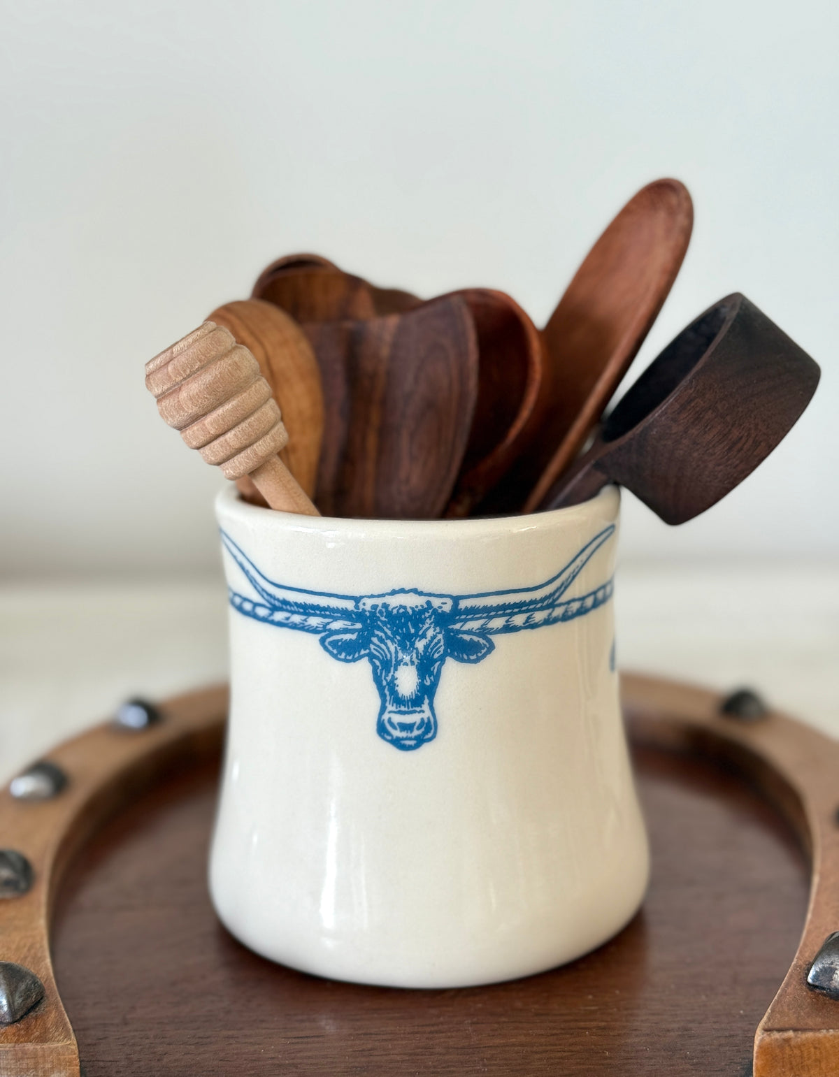 Set of wooden utensils in a white container with blue design on a wooden surface